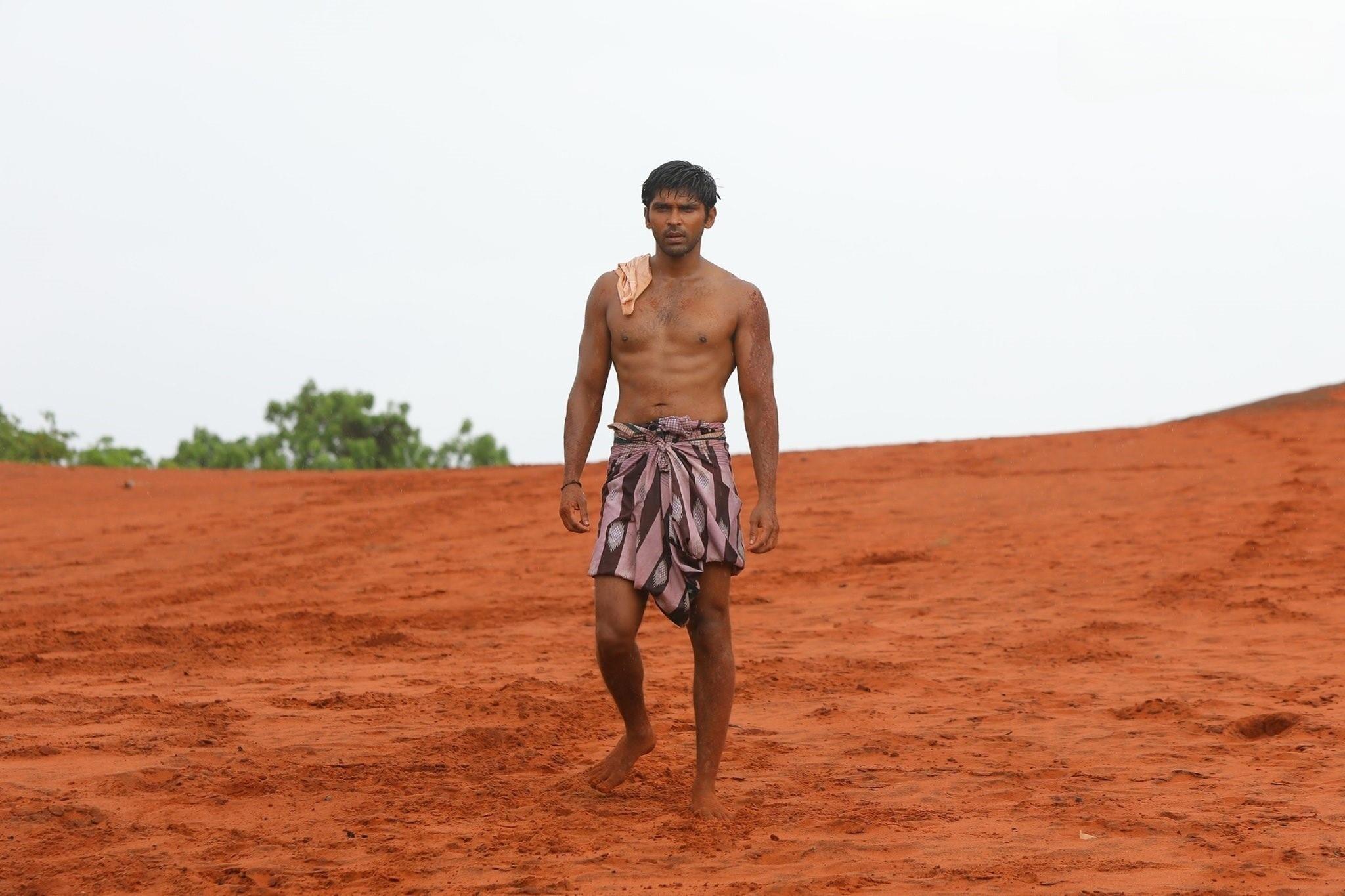 A still of actor Dhruv Vikram standing shirtless in a lungi on vast mud. Kabaddi player Manathi P Ganesan whom Dhruv portrays in Tamil movie Bison used to practice on sand and mud which eventually made him a renowned Kabaddi player in Tamil Nadu, India.